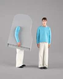 Model standing next to another person wearing a grey upright piano costume against a solid grey background