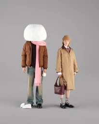 Two models in winter outerwear against a grey backdrop, one wearing a trench coat and beanie, the other with a large snowball head.