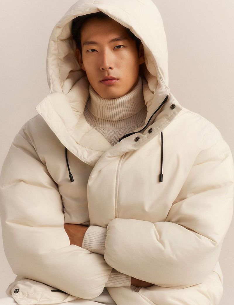 Asian male model wearing a white hooded puffer jacket and turtleneck sweater against a neutral background
