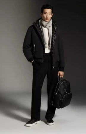 Model Juhyung Kang stands in a black jacket, tailored trousers, grey scarf, and black backpack against a grey studio backdrop.