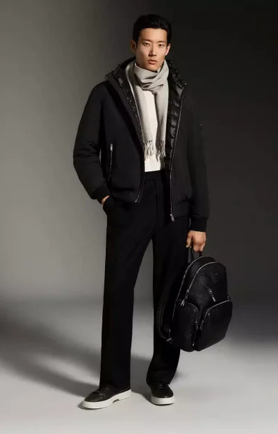Model Juhyung Kang stands in a black jacket, tailored trousers, grey scarf, and black backpack against a grey studio backdrop.