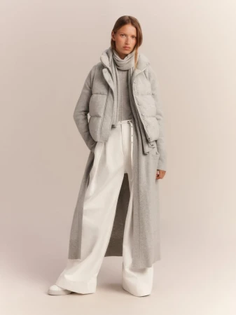 Model Lea Seelenmeyer wearing a grey puffer vest, long knit cardigan, and white wide-leg trousers in a studio shoot.