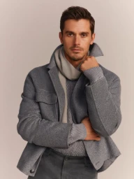 Antoni Porowski wearing a grey wool jacket, textured knit sweater, and scarf against a neutral studio backdrop for BOSS.