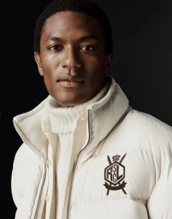 Close-up portrait of a Black man wearing a cream puffer jacket and turtleneck against a dark background