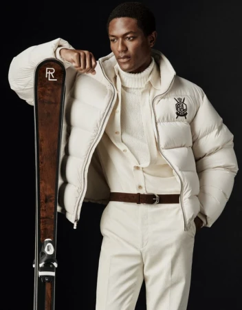 Model wearing a white puffer jacket leaning on skis against a dark background for Ralph Lauren