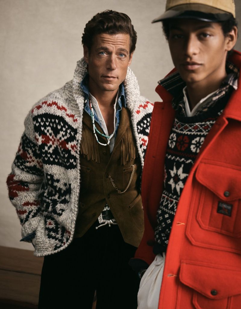 Two adult males pose indoors wearing western and fair isle style clothing, shot at eye-level in a medium studio shot with soft lighting.