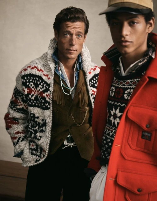 Two adult males pose indoors wearing western and fair isle style clothing, shot at eye-level in a medium studio shot with soft lighting.
