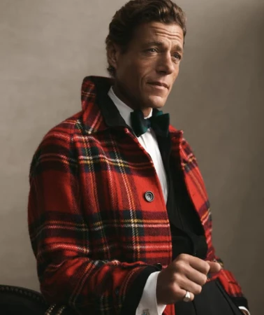 Jon Paul Phillips wearing a red plaid jacket over a white dress shirt and dark bowtie against a neutral studio backdrop.