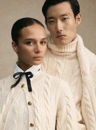Portrait of a man and a woman wearing cream cable-knit sweaters against a neutral background for Polo Ralph Lauren Holiday 2025.