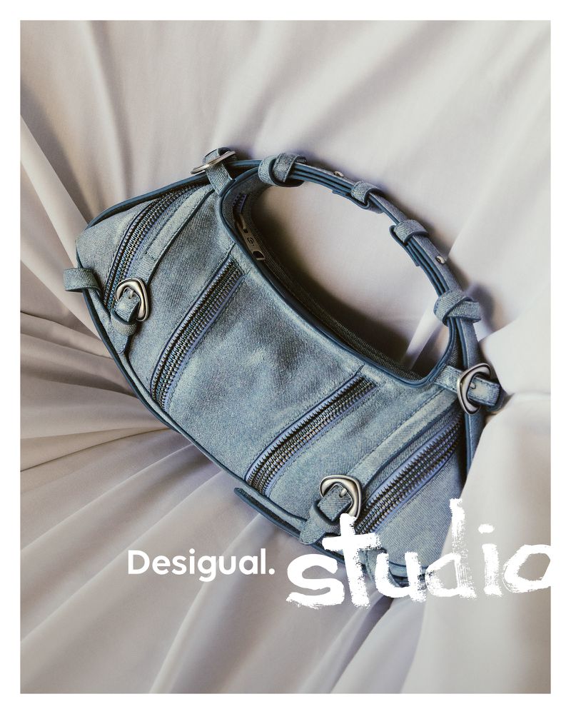 Light blue denim Desigual bag on a light cream colored crumpled fabric backdrop, studio lighting, fashion product shot.