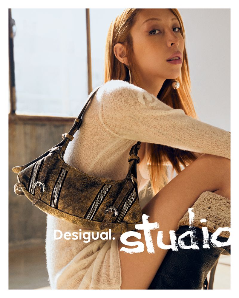 Issa Lish wearing a cream knit dress and holding a distressed brown leather shoulder bag with zipper details for Desigual Studio.