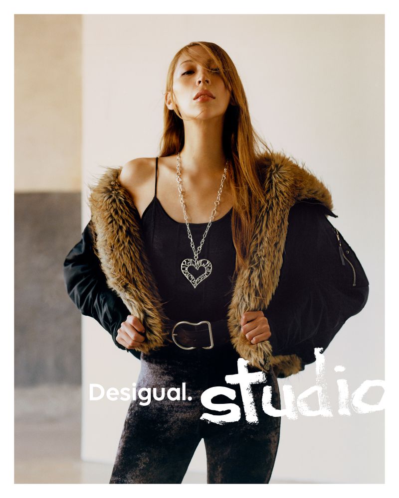 Fashion shot of a woman wearing a fur-trimmed jacket, spaghetti-strap top, and statement necklace, posing in a photo studio with natural light.