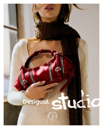 Model Issa Lish holds a textured red shoulder bag with buckle details, styled with a cream knit top and brown chunky scarf.