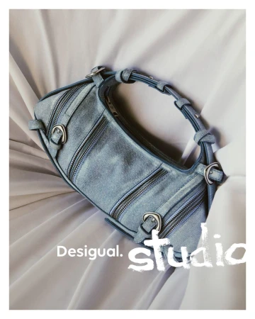 Blue denim barrel handbag with zip details and silver buckles on draped white fabric.
