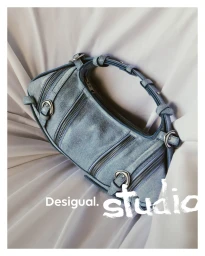 Blue denim barrel handbag with zip details and silver buckles on draped white fabric.