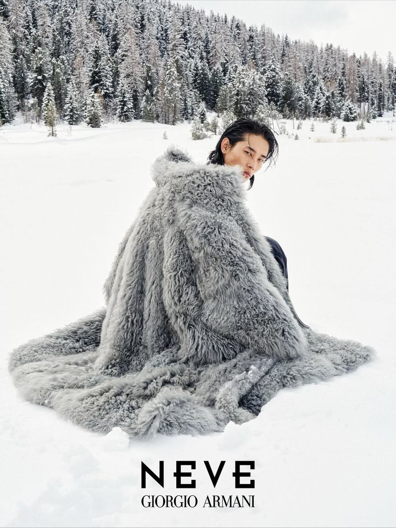 A person in a grey fur coat sits in a snowy outdoor scene, with snow-covered fir trees in the background and fashion text overlay.