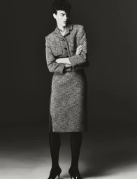 Monochrome fashion portrait of a model with short dark hair standing with arms crossed wearing a tweed skirt suit.