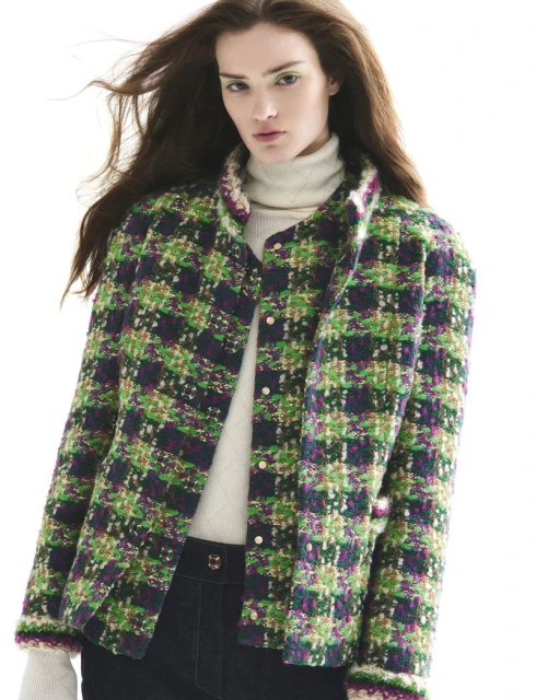 A woman poses in a green, blue, and pink plaid jacket and dark blue jeans against a bright white background in a fashion studio shot.