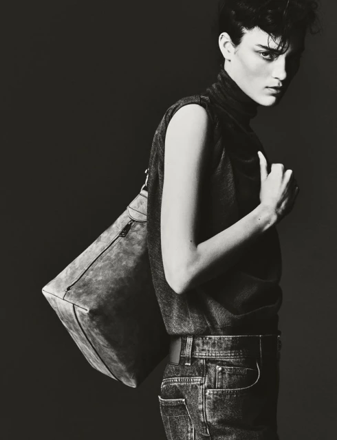 Monochrome portrait of a person with short dark hair wearing a sleeveless top and jeans, carrying a large shoulder bag.