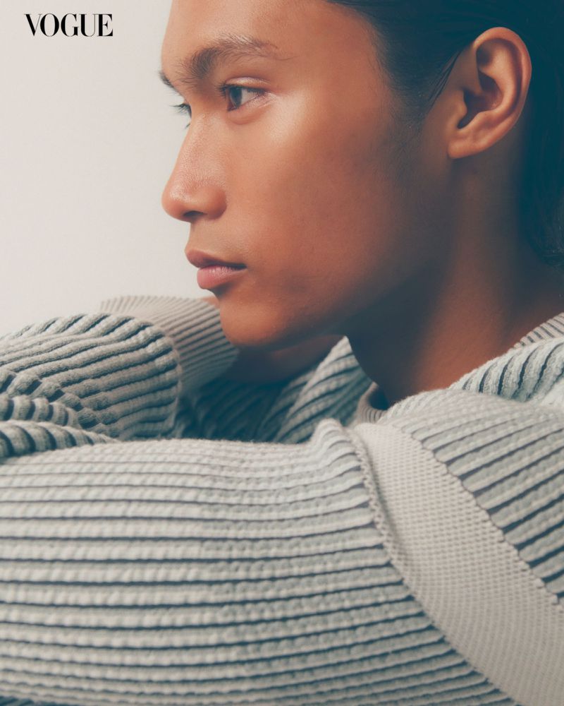 Close-up fashion shot: young male model wearing striped sweater in studio, photographed for Vogue, showcasing neutral tones and clean lines.