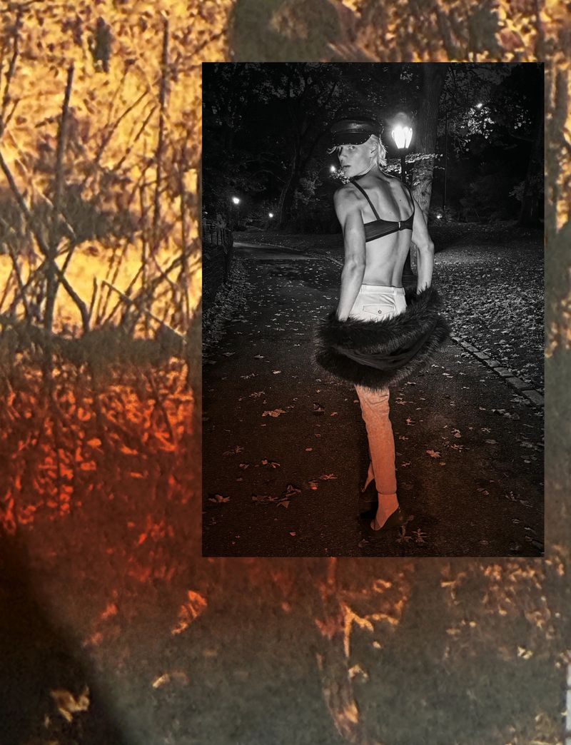 A person in lingerie and a fur stole stands on a path at night, framed against a blurred foliage background for high fashion.