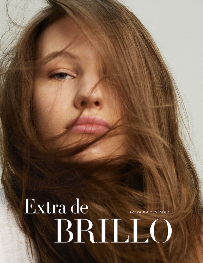 Close-up portrait of a woman with light brown hair, light skin, and pink lips against a neutral background, showcasing beauty and editorial fashion.