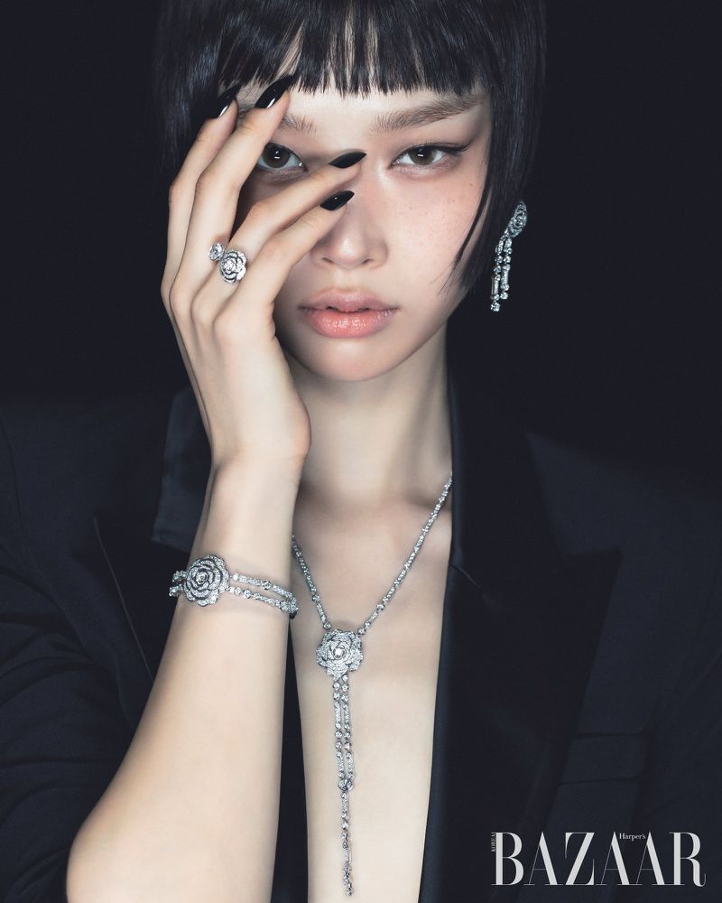 Close-up fashion shot of an adult female wearing a black blazer and flower-themed diamond jewelry, including a necklace, bracelet, ring, and earrings.