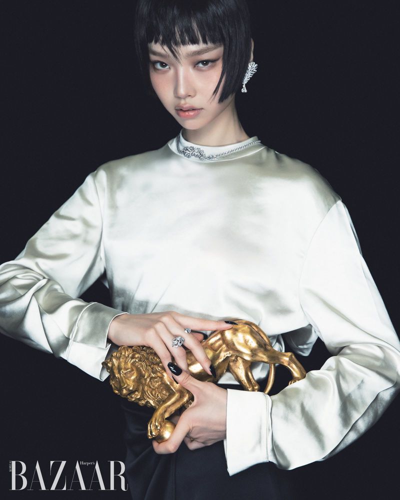 Asian woman with short black hair posing with a gold lion sculpture against a dark background for a fashion editorial layout.