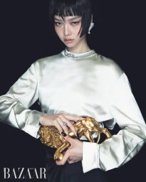 Model wearing a white silk blouse holding a gold lion sculpture against a black background for Harper's Bazaar Korea