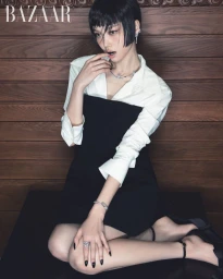 Model with dark bob hairstyle wearing a white shirt and black dress with Chanel high jewelry against a wooden wall