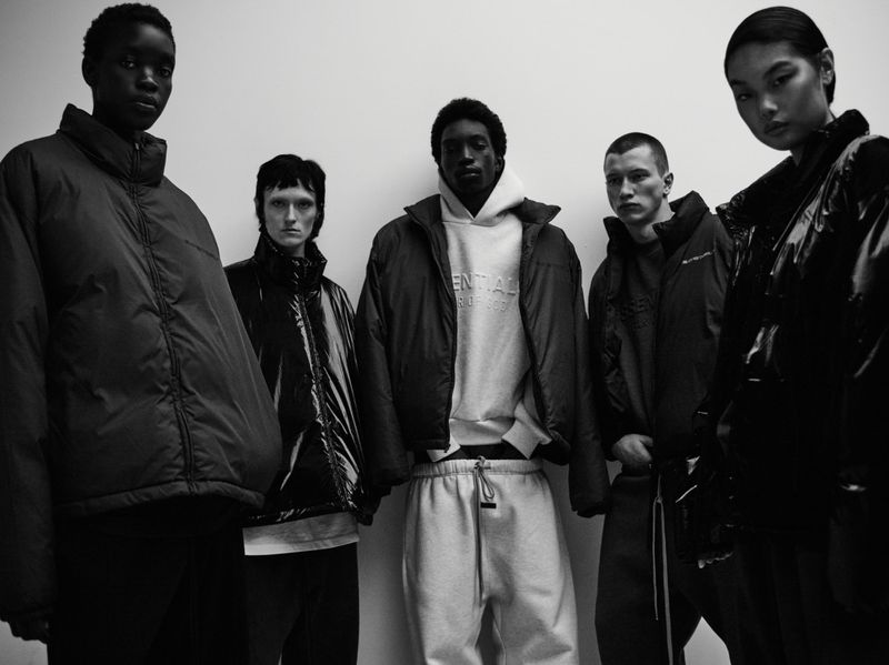 Five diverse models stand in front of a white wall, showcasing fashion apparel: a puffer jacket, hoodie, and sweatpants in a studio setting.