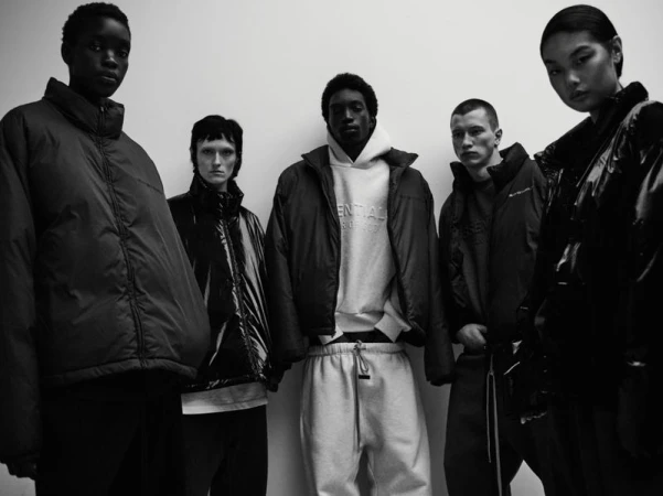Five models posing together against a plain background in a black and white fashion portrait for Fear of God Essentials.