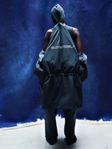 Model seen from behind wearing dark hooded outerwear with text graphic against a textured blue backdrop