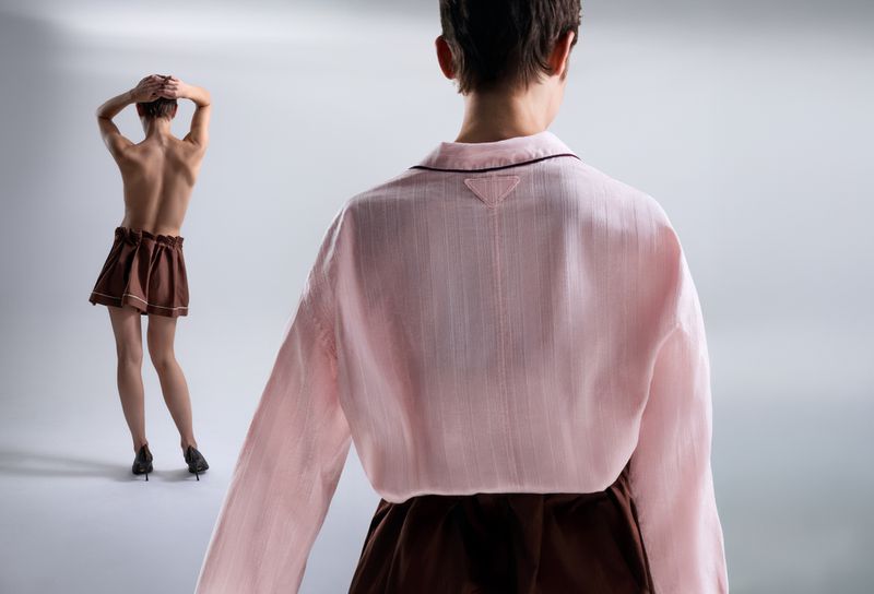 Two back-facing women in studio lighting. One woman in a pink top and brown skirt is close to the camera; the other is further away.
