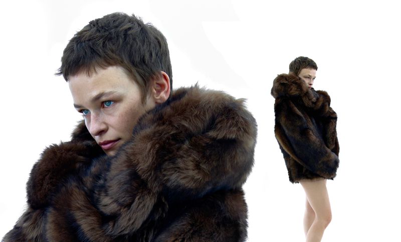 Elegant fashion shot featuring a woman with short dark hair wearing a brown fur coat against a pure white background in a studio setting.