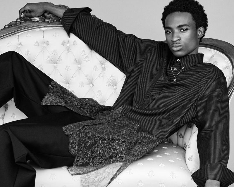 Elegant studio portrait of an African-American man in a striped shirt and black pants, reclining on an ornate white chaise lounge.