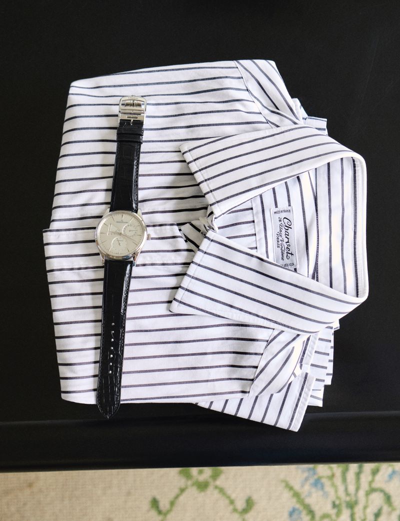 A neatly folded striped shirt sits next to a silver wristwatch with a black band, all placed on a dark surface with neutral-toned decor.