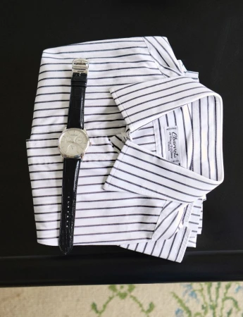 A neatly folded striped shirt sits next to a silver wristwatch with a black band, all placed on a dark surface with neutral-toned decor.