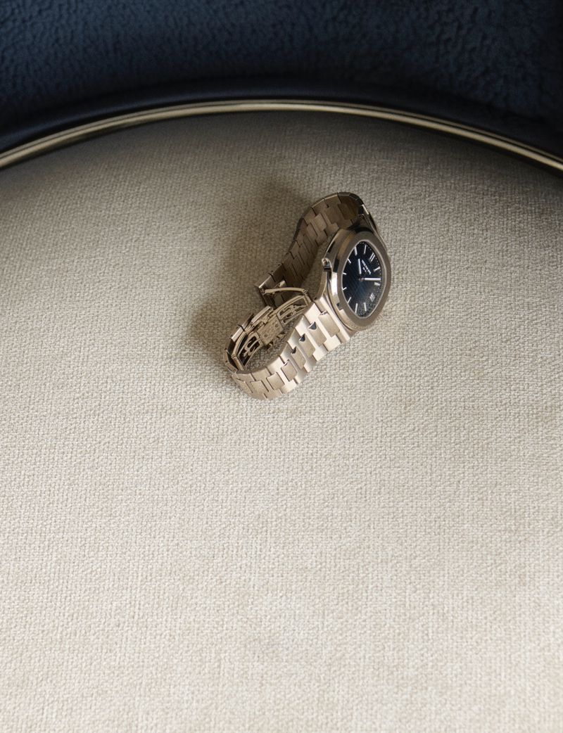 Silver wristwatch with a blue face and metal band, studio shot on a light grey textured surface.