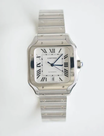 Elevated studio shot of a silver Cartier Santos wristwatch with a square face, Roman numerals, and blue hands on a white background.