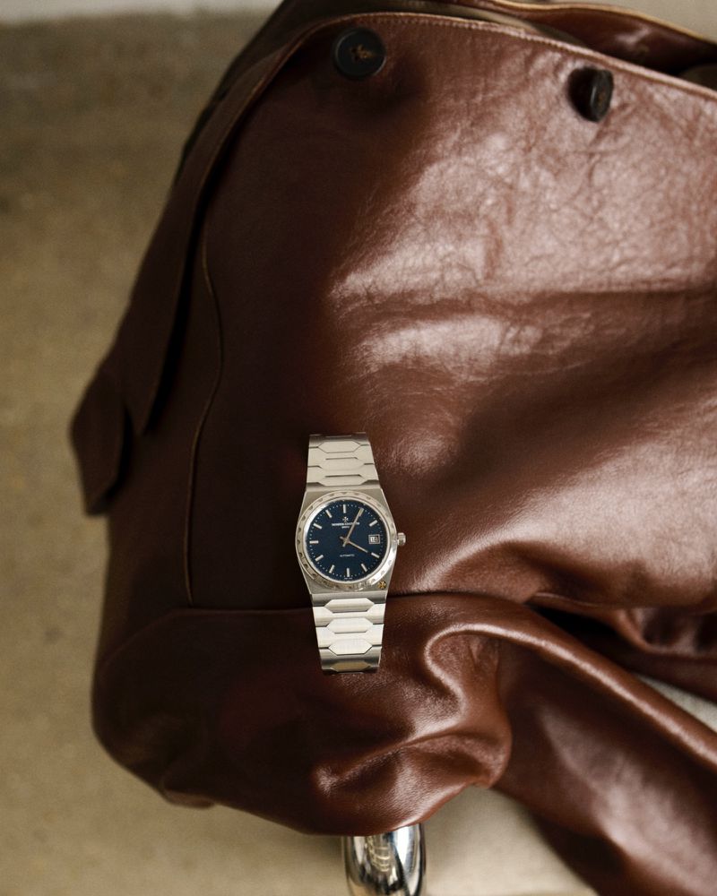 Close-up of a silver wristwatch with a blue face resting on a brown leather jacket, emphasizing luxury, style, and attention to detail.