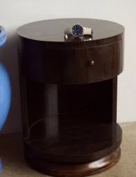 Silver wrist watch with a blue face resting on a dark wood round bedside table next to a blue ceramic vase.