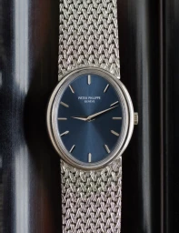 Patek Philippe wristwatch with a blue dial and silver mesh bracelet photographed vertically against a dark wooden background