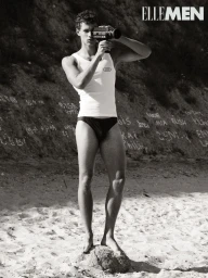 Monochrome fashion portrait of a model holding a vintage movie camera standing on a rock at the beach for Elle Men Thailand