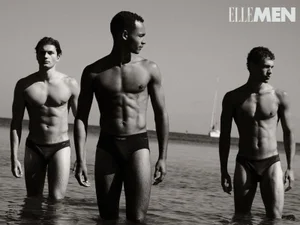 Three shirtless male models wearing briefs standing in shallow coastal water under bright daylight for Elle Men Thailand.