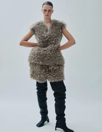 Model wearing textured brown fleece top and matching shorts with black knee high leather boots against a white studio background.