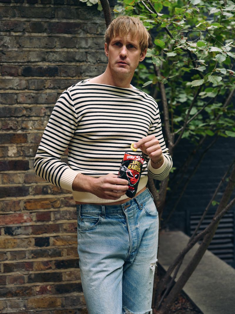 Adult male in striped shirt outdoors holds chips in an urban location, showcasing a blend of casual style and snack food.