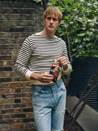 Adult male in striped shirt outdoors holds chips in an urban location, showcasing a blend of casual style and snack food.