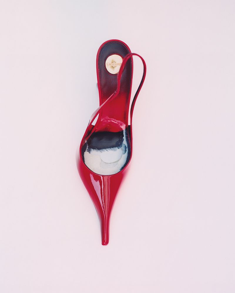 Overhead studio shot of a single red slingback heel shoe against a pale pink background, showcasing a pointed toe and minimalist design.