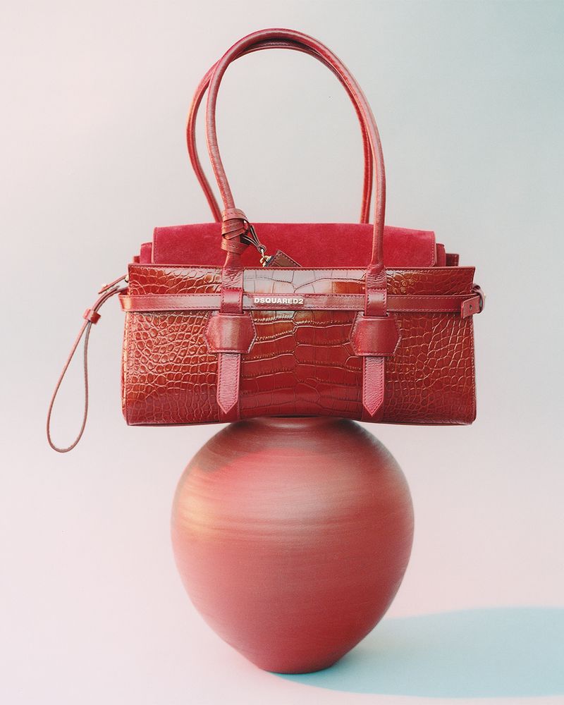 Elegant red leather handbag on a matching vase, creating a stylish fashion product shot with a clean studio background.